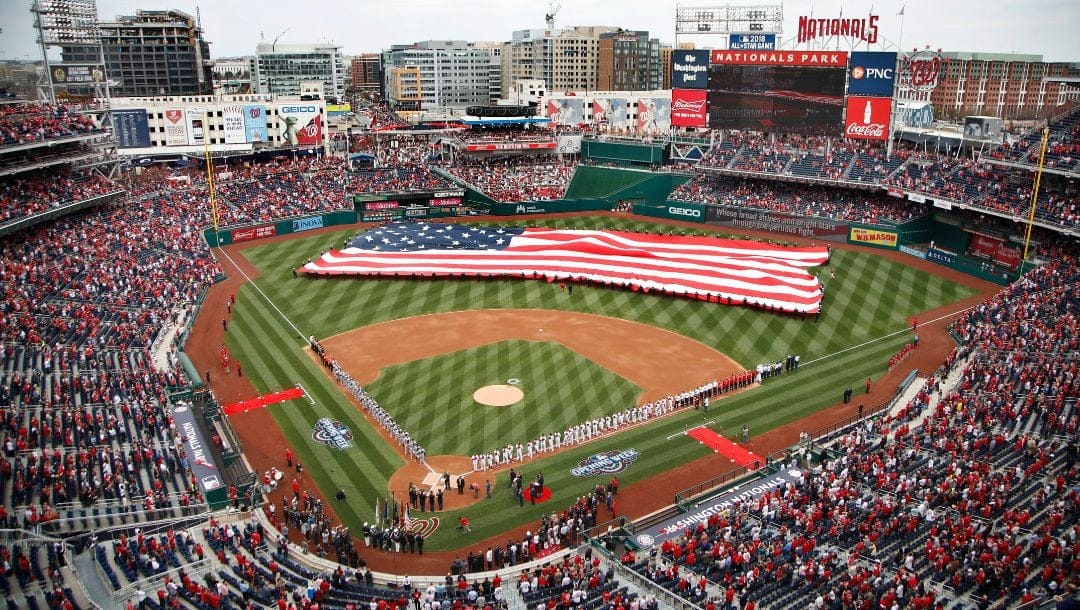 Service members of the United States Armed Forces unfurl a giant American flag covering the baseball diamond.