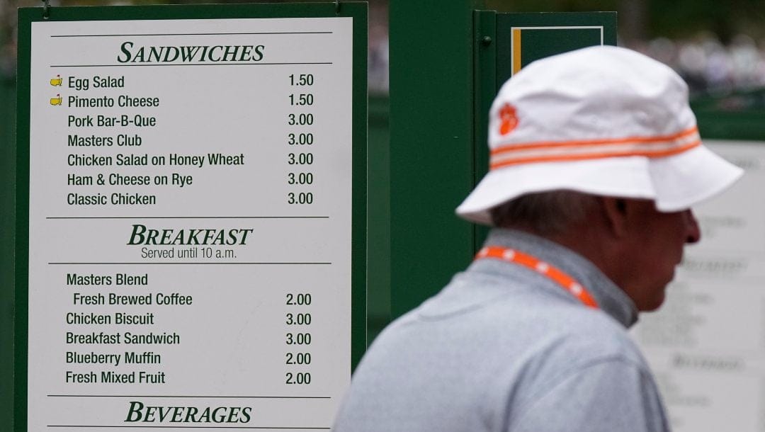 A patron walks past a sign displaying the prices of food items during a practice round in preparation for the Masters golf tournament at Augusta National Golf Club Tuesday, April 9, 2024, in Augusta, Ga.
